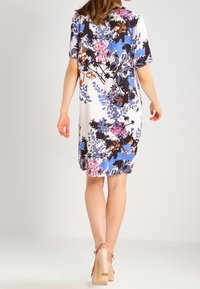 Vestido floral hasta la rodilla en tela blanca con patrones en azul, rosa y negro. Textura suave, con mangas cortas y corte holgado.