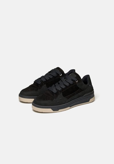 Paire de baskets basses noires avec des lacets gris foncé et des semelles beige sur fond blanc uni.