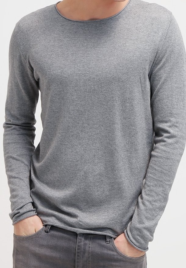 Maglietta grigia a maniche lunghe realizzata in tessuto morbido, con scollatura a girocollo e maniche aderenti, presentata con le mani in tasca su uno sfondo semplice.