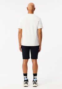 T-shirt bianco a maniche corte, pantaloni corti blu navy, calze nere a fantasia con dettagli blu, e sneakers bianche con dettagli grigi.
