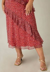 Röd blommig kjol med volangkant, gjord av lättviktig tyg. Har små mångfärgade blommor och genomskinligt överdrag. Matchas med guldklackar.