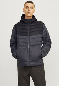 Black puffer jacket with a zip front, hood, and chevron quilted design. Made from lightweight, shiny material; features elastic cuffs.