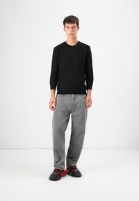 Pulover negru cu mâneci lungi și potrivit, blugi gri largi, pantofi sport negri cu accente roșii, stând pe un fundal alb. Design minimalist.