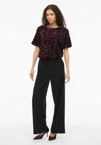 Burgundska bluza s sequins z kratkimi rokavi, v kombinaciji s črnimi širokimi hlačami in pete. Bluza ima teksturirano, sijočo površino.