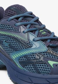 Scarpa atletica blu navy con tomaia in mesh e sintetico. Presenta accenti verdi, sovrapposizioni testurizzate e lacci piatti. Suola in gomma con grip a motivo.