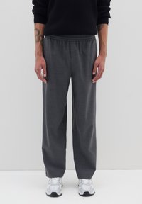 Graue weite Hosen aus weichem Stoff, mit einem elastischen Bund und einer glatten Textur. Kombiniert mit weißen Sport Schuhen.