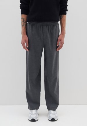 Grijze brede broek gemaakt van zacht materiaal, voorzien van een elastische tailleband en een gladde textuur. Gecombineerd met witte sportschoenen.