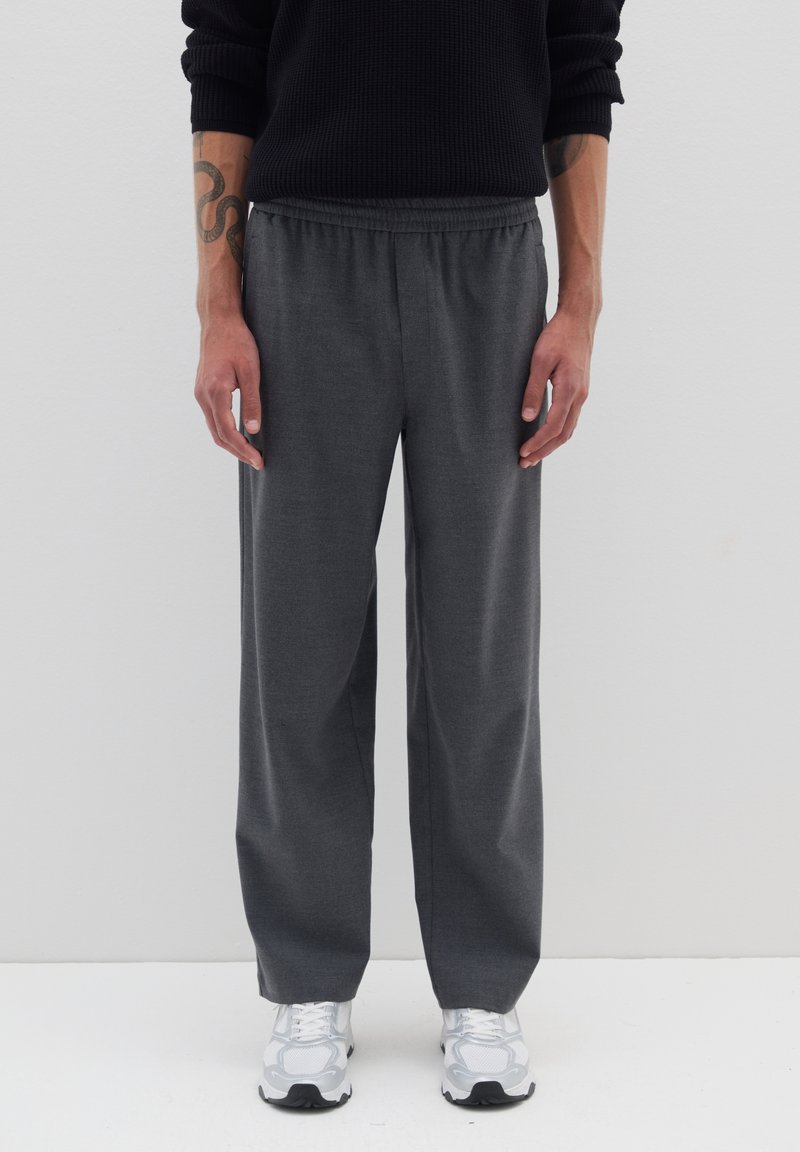 Graue weite Hosen aus weichem Stoff, mit einem elastischen Bund und einer glatten Textur. Kombiniert mit weißen Sport Schuhen.