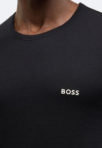 T-shirt nera a girocollo in morbido cotone, con logo "BOSS" bianco ricamato sul petto a sinistra. Texture liscia, design aderente.