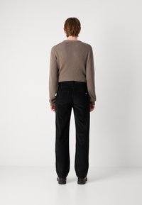Brown ribbed long-sleeve shirt paired with black corduroy pants, featuring two back pockets and a subtle logo detail. Matte finish.