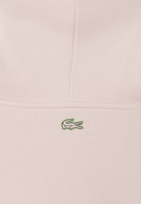 Sudadera rosa claro con una tela texturizada, puños acanalados y un pequeño logotipo de cocodrilo verde bordado en el pecho.