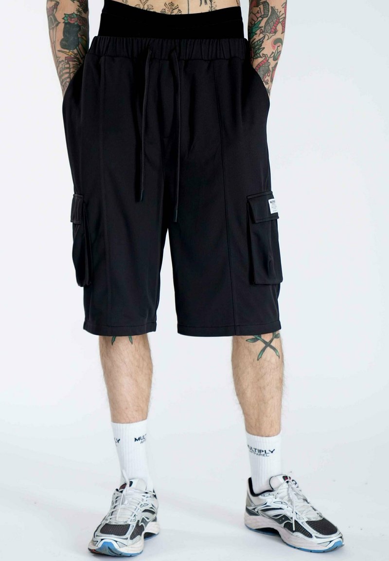 Pantaloni cargo neri con elastico in vita, dotati di due tasche laterali e una tasca applicata sulla destra. Realizzati in tessuto leggero e morbido.