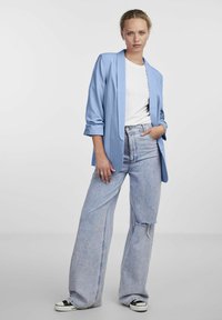Blazer azzurro chiaro con maniche arrotolate, indossato su una maglietta bianca. Abbinato a jeans in denim azzurro chiaro a vita alta e scarpe sportive nere.