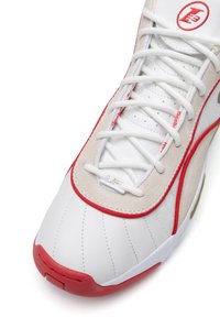 Biely teniska s červenými akcentmi, vyrobená z hladkej kože a semišu, so šitými detailmi, okrúhlymi šnúrkami a kovovým logom na jazyku.