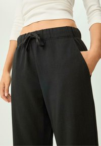 Schwarze Jogginghosen mit Kordelzugbund und Seitentaschen. Der Stoff wirkt weich, hat einen lockeren Schnitt und eine glatte Textur.