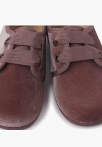 Scarpe di velluto in un mauve tenue con punta arrotondata, dotate di doppio lacci elastici e occhielli, tessuto testurizzato e una suola morbida e flessibile.