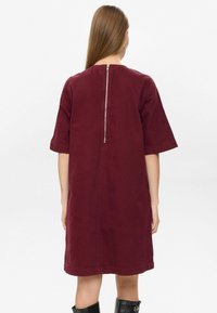 Burgundin värinen puuvillamekko lyhyillä hihoilla, takanasta suljettuna ja rentona istuvana. Helma päättyy polven yläpuolelle. Sileä pinta, minimalistinen muotoilu.