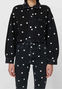 Czarna denimowa kurtka i spodnie z białymi haftami stokrotek, o krótkim kroju, z zapięciem na guziki i kieszeniami, tworzące spójną całość.