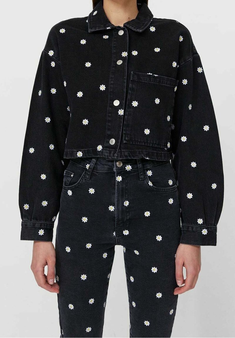 Czarna denimowa kurtka i spodnie z białymi haftami stokrotek, o krótkim kroju, z zapięciem na guziki i kieszeniami, tworzące spójną całość.