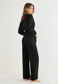 Svart tvådelat outfit i mjuk stickad tyg; har en avslappnad topp med långa ärmar och vida byxor.