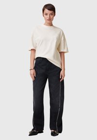 Camiseta de manga corta color crema con un gráfico sutil, combinada con pantalones vaqueros negros de corte alto y pierna ancha, con costuras laterales metálicas con tachuelas.