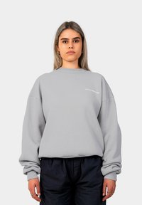 Gaiši pelēks, pārāk liels sporta krekls ar ribinātu apkakli un piedurknēm, uz krūškurvja ir balts teksts "PROHIBITED". Mīksta auduma tekstūra.