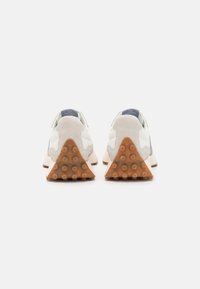 Zapatillas con una parte superior de ante blanco, acentos grises y una suela de goma color caramelo con un patrón texturizado y con puntos. La vista trasera muestra un tacón triangular.
