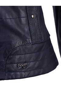 Marineblaue Lederjacke mit subtiler Textur, diagonal genäht und mit einem kleinen metallischen Logoakzent. Nahaufnahme von der Seite.