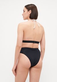 Black bikini set featuring a halter top with a white tie and high-waisted bottoms. Smooth texture, minimal design, and adjustable straps.