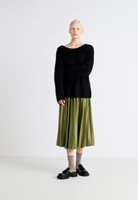 Black knitted sweater, green pleated midi skirt, sheer striped socks, and black platform shoes. Smooth texture, relaxed fit, and layered design.