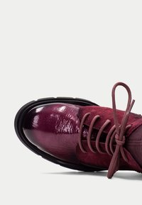 Zapato de cuero burdeos con un acabado brillante, parte superior de ante y acentos texturizados. Presenta una puntera redonda y un diseño de cordones con una suela negra en contraste.