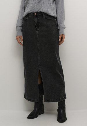 Gonna maxi in denim nera con uno spacco frontale, vita alta e dettagli di cucitura visibili. Abbinata a stivali cowboy neri e un maglione grigio.