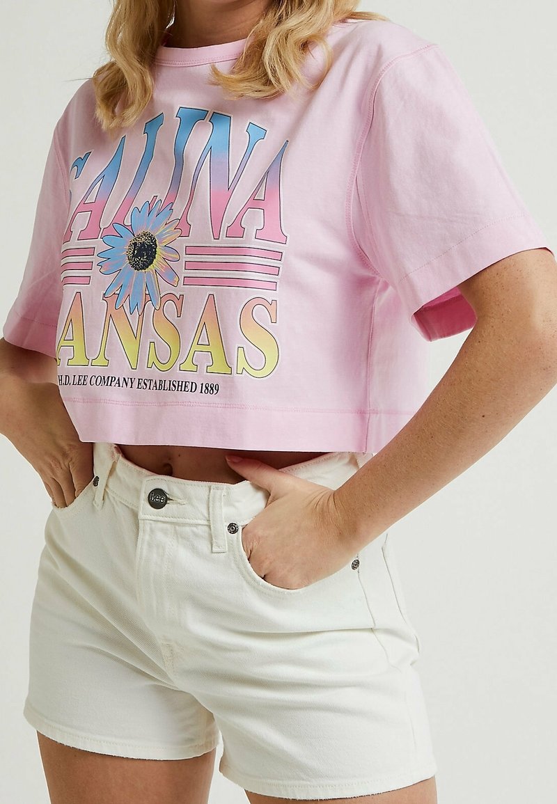 Vaaleanpunainen lyhythihainen t-paita, jossa on monivärinen graafinen teksti ja kukkakuvio; yhdistetty valkoisiin farkkushortseihin, joissa on sivutaskut ja hopeiset yksityiskohdat.