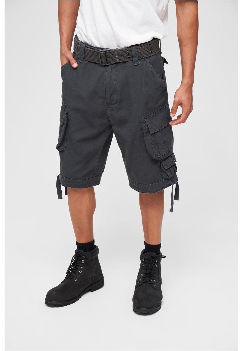 Homme portant un short cargo noir avec poches latérales, ceinture noire, chaussettes noires et bottines noires à lacets, debout sur un fond clair.