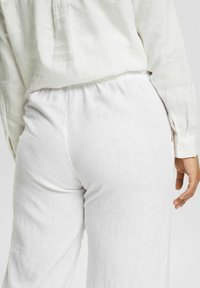 Vita linnbyxor med elastisk midja, med en avslappnad passform, texturerad tygkvalitet och en enkel design. Slät yta och minimala detaljer.