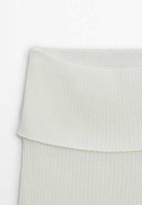 Tessuto a coste di colore crema con una vita ripiegata. La texture appare morbida, con linee verticali che creano un motivo sul materiale.