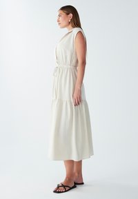 Helebeež suurte õlavarreteta kleit, millel on vöötatud talje, kihiline seelik ja nööpdetailid. Kombineeritud mustade sussidega.