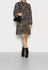 Brown, textured dress with black abstract pattern, long puff sleeves, high neck, and buttons. Paired with black ankle boots and handbag.