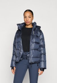 Navy puffer jacket with a shiny finish, quilted design, and detachable hood. Features a front zipper and fitted cuffs. Worn with a black top.