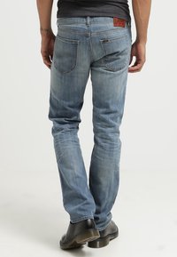 Vaqueros de denim azul claro con corte ajustado, cuentan con bolsillos traseros, un ligero desgaste y una etiqueta de marca de cuero en la cinturilla.