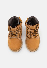Braune Wildleder-Stiefeletten mit schwarzen Schnürsenkeln, gepolsterter Knöchelkante und weißen Nähten an der Seite. Reißverschluss auf einer Seite.