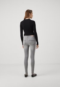 Svart långärmad ribbad topp som kombineras med åtsittande grå denimjeans, som har en subtil blekning och två bakfickor, kompletterat med spetsiga svarta skor.