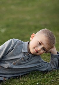 Jasnoszara koszula z długim rękawem i kołnierzykiem, z drewnianymi guzikami. Poziome przeszycia i miękka tekstura. Dziecko leży na trawie.