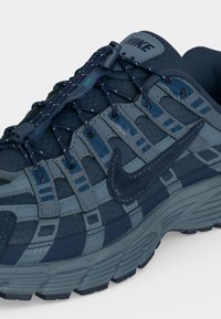 Αθλητικό παπούτσι Nike σε ναυτικό μπλε με ανώτερο μέρος από διχτυωτό υλικό, συνθετικές επικαλύψεις, ανακλαστικά κορδόνια και χονδρή εξωτερική σόλα με βαθιά ανάγλυφα, σχεδιασμένο για ορεινό τρέξιμο.