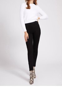Pantalons noirs taille haute avec une finition lisse, associés à un pull moelleux blanc et des bottes de cheville à motif serpent.