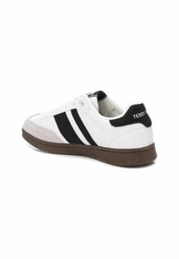 Zapatilla deportiva blanca con rayas negras en el lateral, una suela texturizada y un acento en el talón negro con el texto "TEDDY".