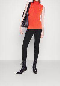 Haut en col roulé sans manches à rayures rouges associé à des leggings noirs et des bottes à talons avec un bout pointu et des accents métalliques. Sac à épaule noir.