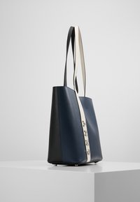 Läderhandväska med en marinblå framsida, svart baksida och ett krämfärgat rem med silverdetaljer och logotyp.