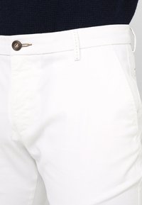 Witte katoenen broeken met een knoopsluiting in de taille, voorzakken en een gladde textuur. Het ontwerp is op maat gemaakt en minimalistisch.