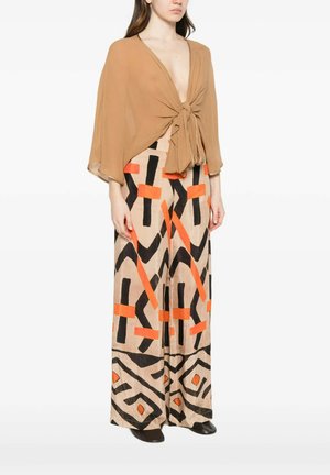 Donna che indossa una camicetta color tacco con scollo profondo a V annodata davanti e pantaloni a gamba larga con motivi geometrici astratti neri e arancioni.